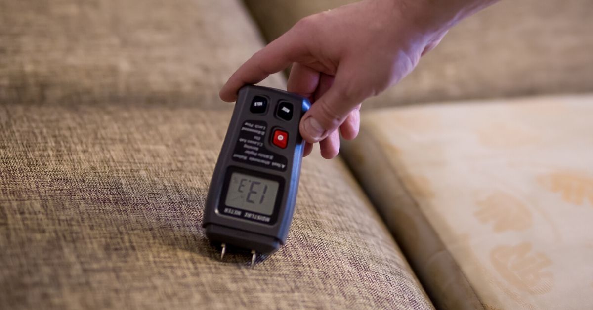 Man mäter fukt i soffa med digital fuktmätare