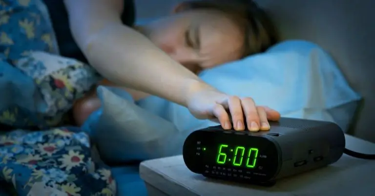 Kvinna vaknar i sängen och stänger av sin klockradio