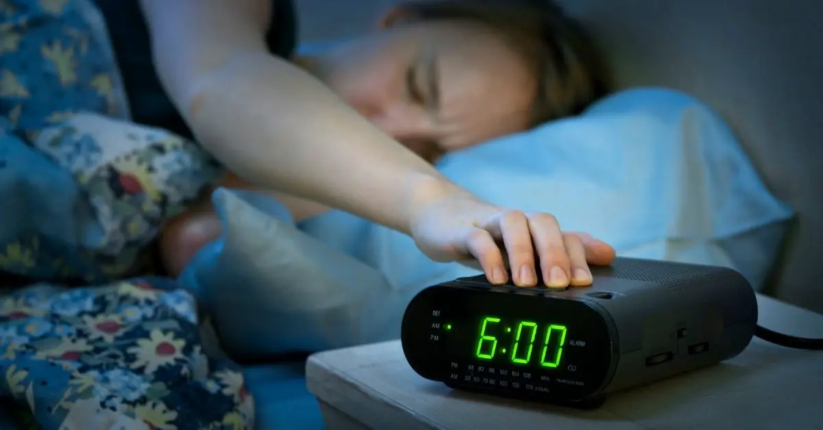 Kvinna vaknar i sängen och stänger av sin klockradio