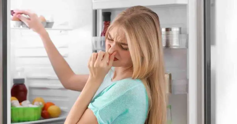 Blond kvinna öppnar kylskåpet och håller för näsan på grund av dålig lukt